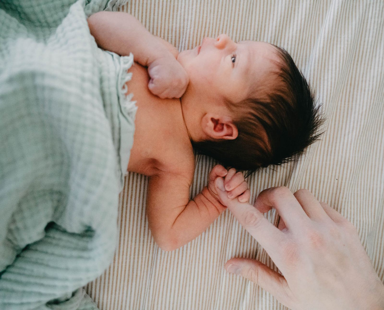 Newborn baby resting on a blanket with a parent's hand nearby