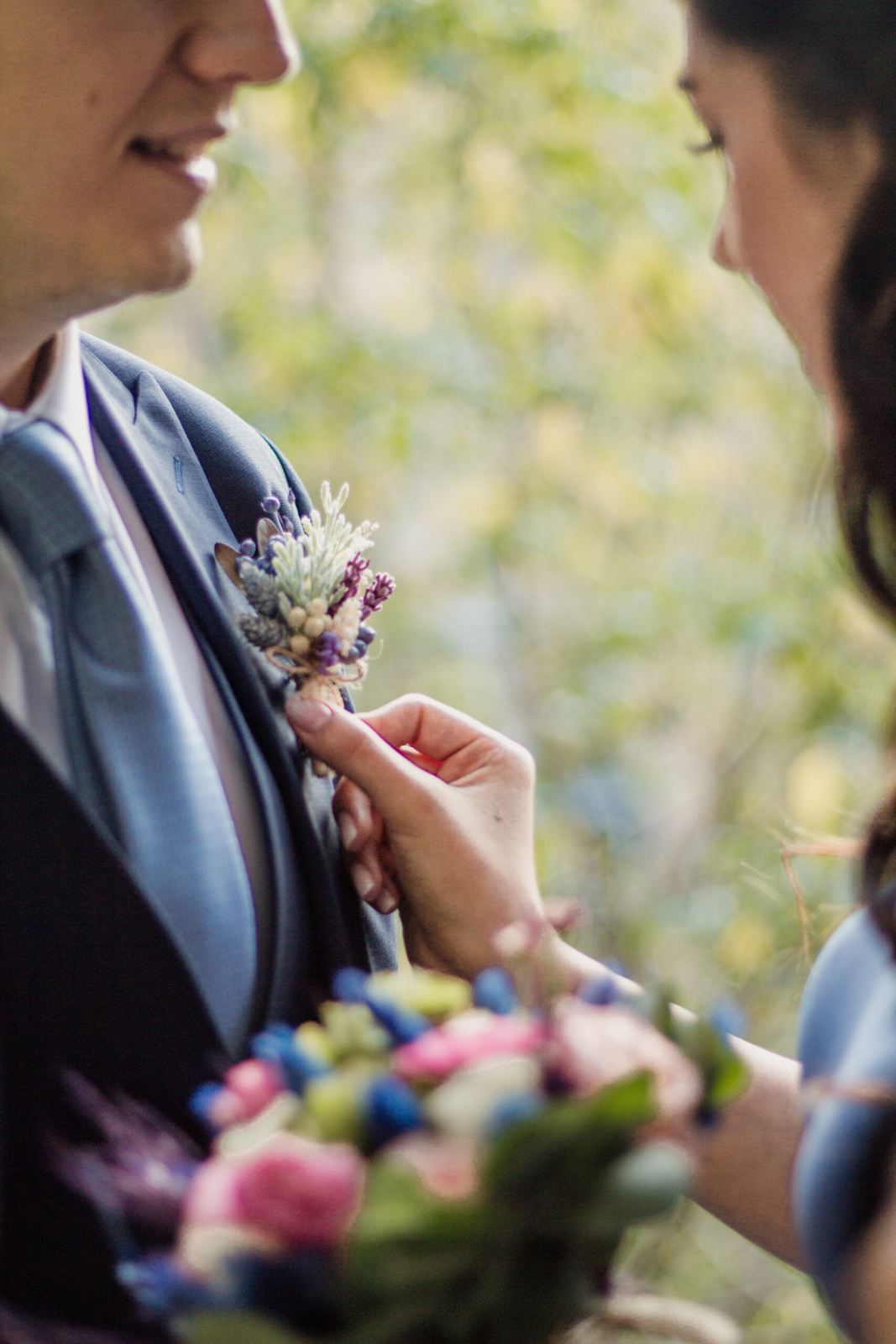 Bride pinning a boutonniere on the groom's jacket, bouquet in the foreground