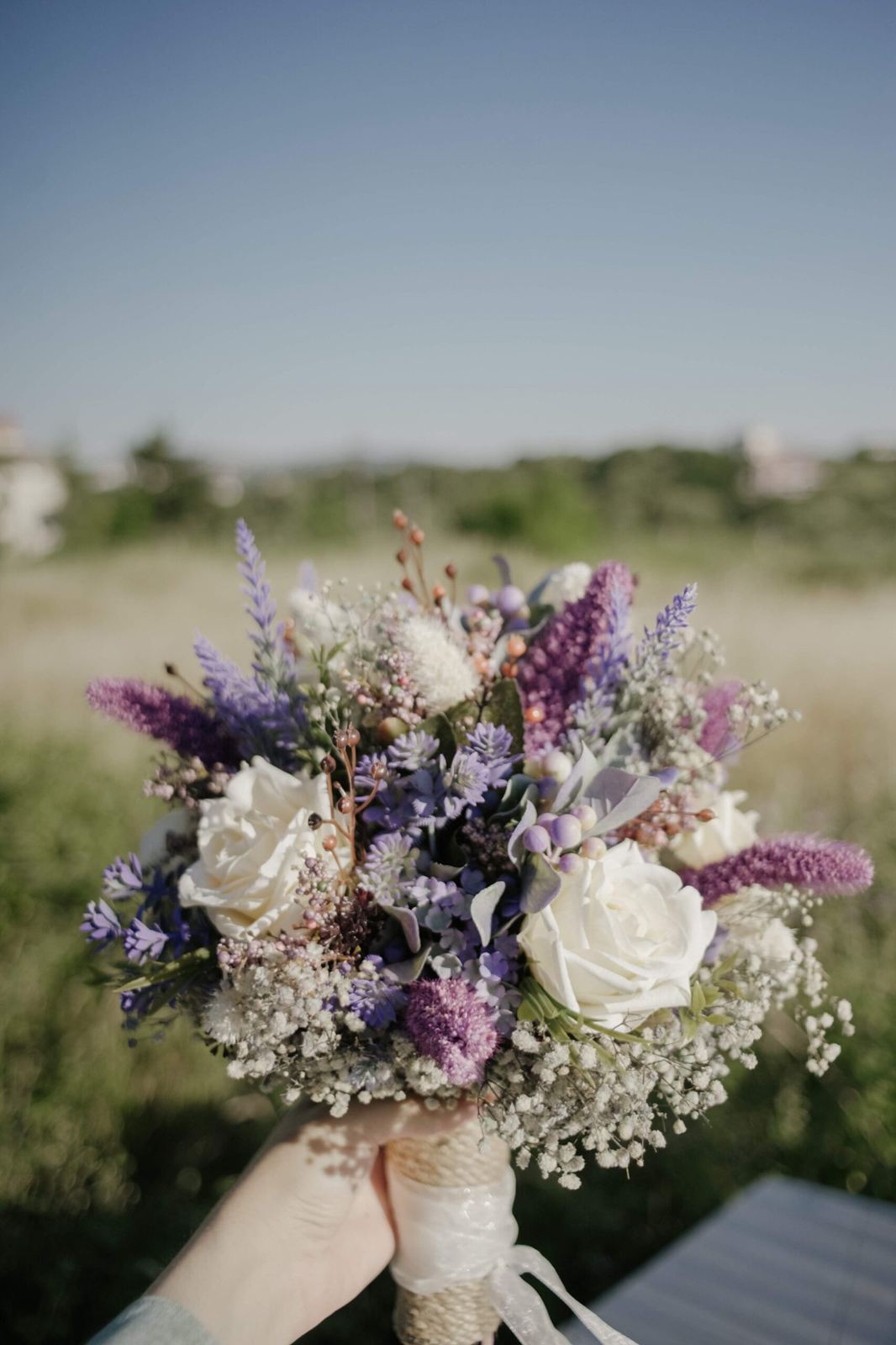 Bridal bouquet of lavender and white flowers held up outdoors